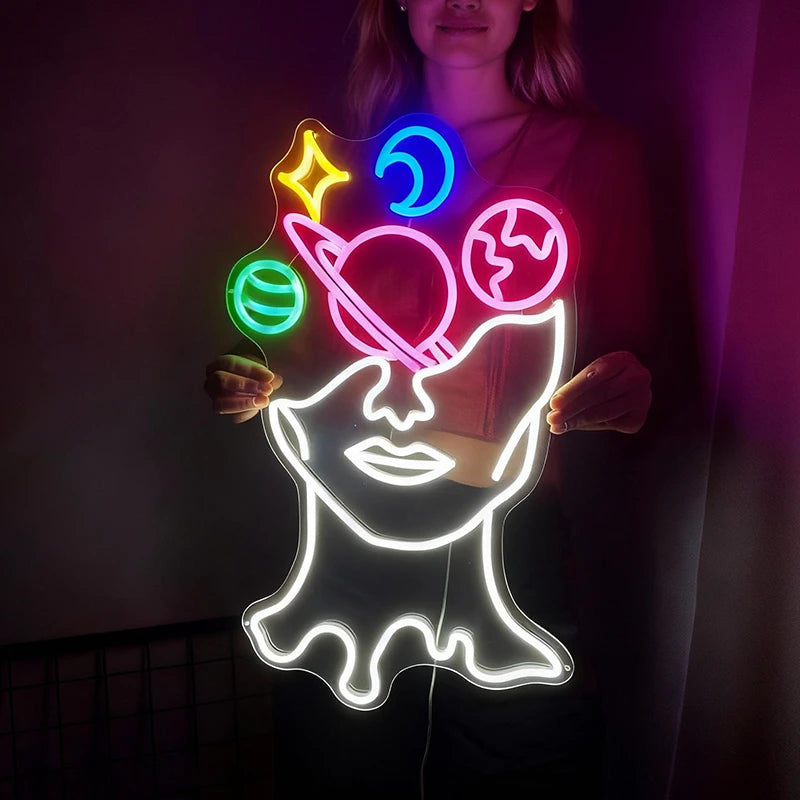 Neon sign of a face with galaxy symbols held by a person in a dark setting