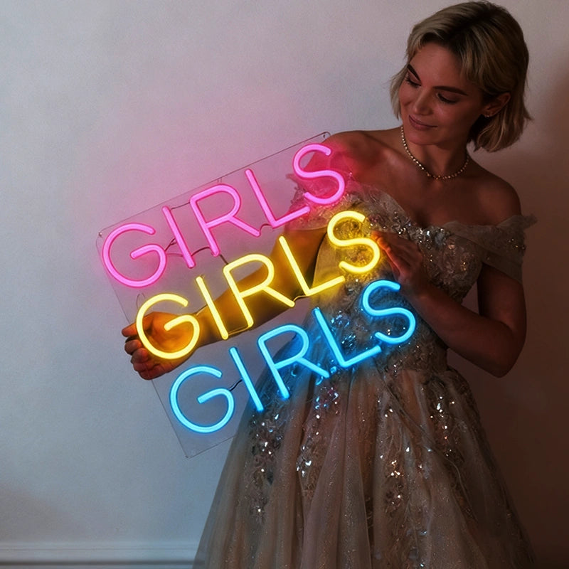 Woman holding a neon sign with 'GIRLS GIRLS GIRLS' in hot pink, lemon yellow, and blue.
