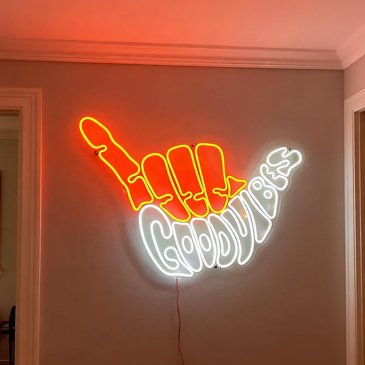 Neon sign shaped like orange light fingers with white 'Good Vibes' text on a wall.