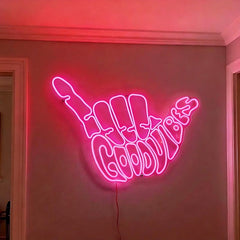 Pink neon sign shaped like a hand with 'Good Vibes' on a wall.