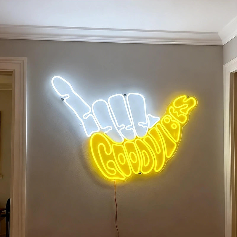 Neon sign shaped like white light fingers with yellow 'Good Vibes' text on a wall.
