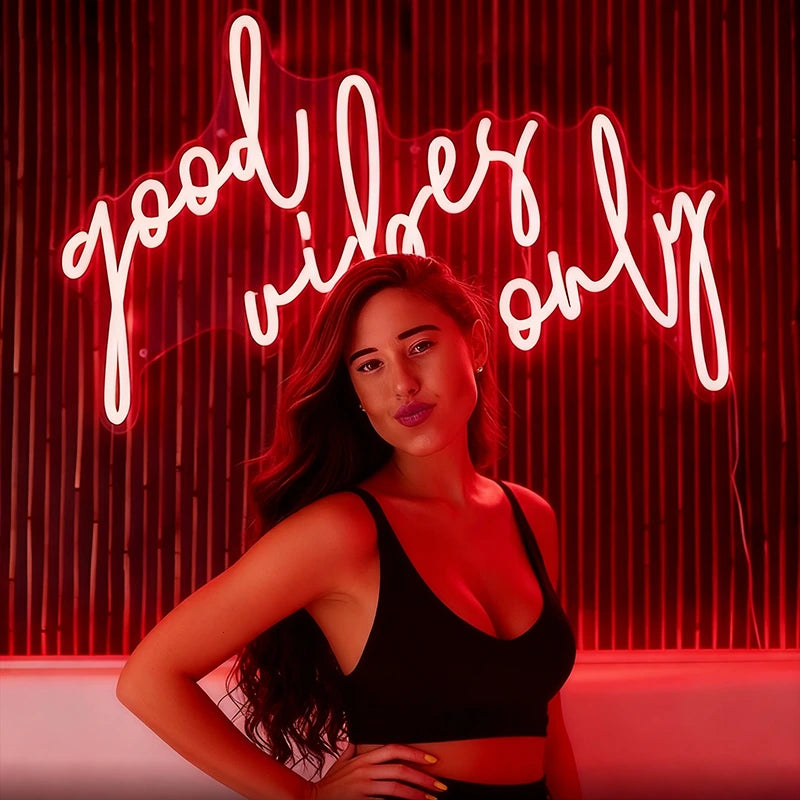 Woman posing in front of a red neon sign with the text 'good vibes only' on a red curtain background.