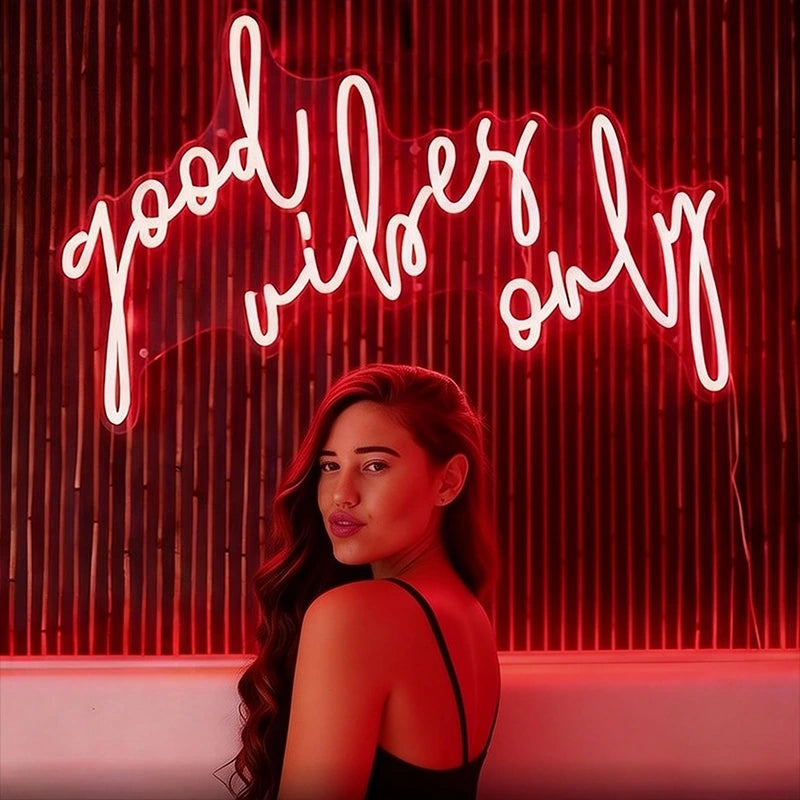 Woman standing in front of a red neon sign with 'good vibes only' text.