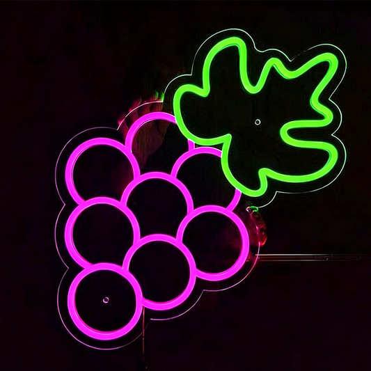 Person holding a neon sigh shaped like grapes with and green leaves on a black background.