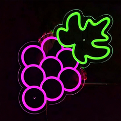 Person holding a neon sigh shaped like grapes with and green leaves on a black background.