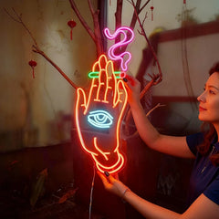 Neon sign of a hand with eye and smoking held by a person, with a blurred background.