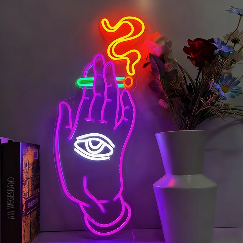 Neon sign of a hand with an eye and smoking above it, next to a vase with flowers.