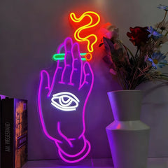 Neon sign of a hand with an eye and smoking above it, next to a vase with flowers.
