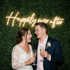 Couple celebrating with champagne in front of a 'Happily ever after' sign.