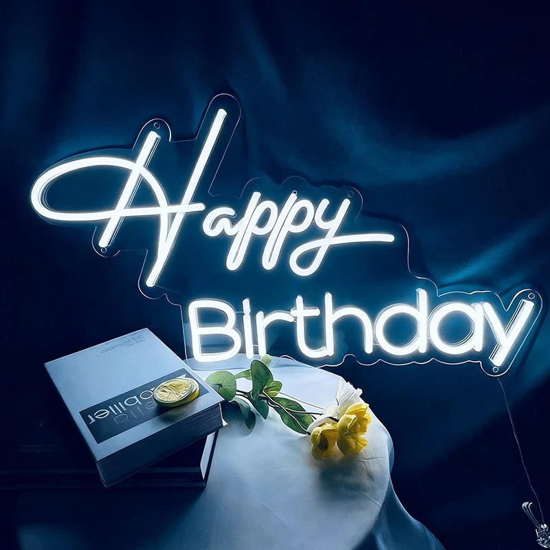 Neon 'Happy Birthday' sign with a box and flowers on a dark background