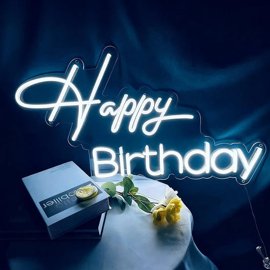 Neon 'Happy Birthday' sign with a box and flowers on a dark background