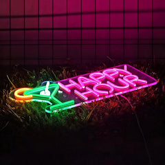 Neon sign with 'Happy Hour' on grass against a tiled wall