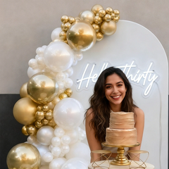 Hello Thirty neon sign displayed on a white party backdrop with white and gold balloon garland for a 30th birthday celebration.