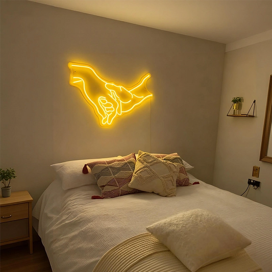 Neon light shaped like two hands holding hands above a bed in a bedroom.