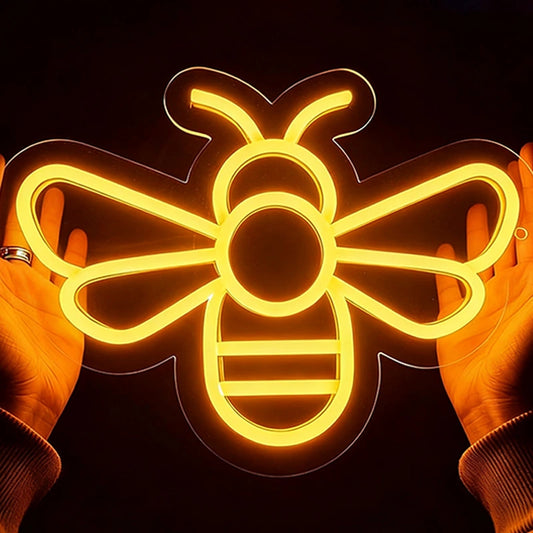 Neon bee light held between two hands against a dark background