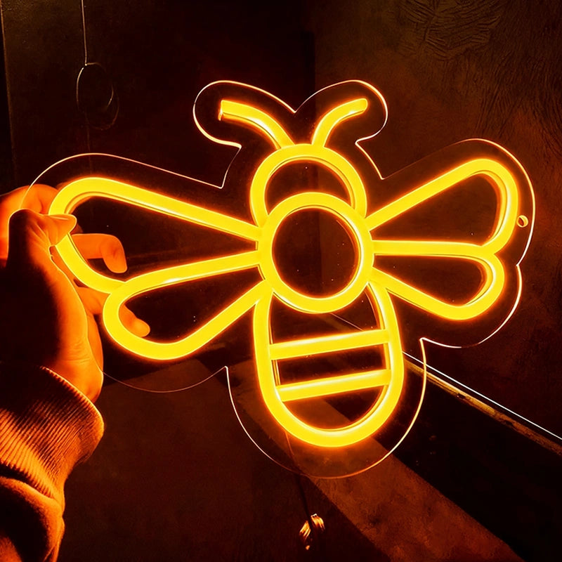 Neon bee-shaped light held by a hand against a dark background