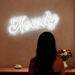 Person sitting in front of a 'Howdy' neon sign on a warm-toned wall.