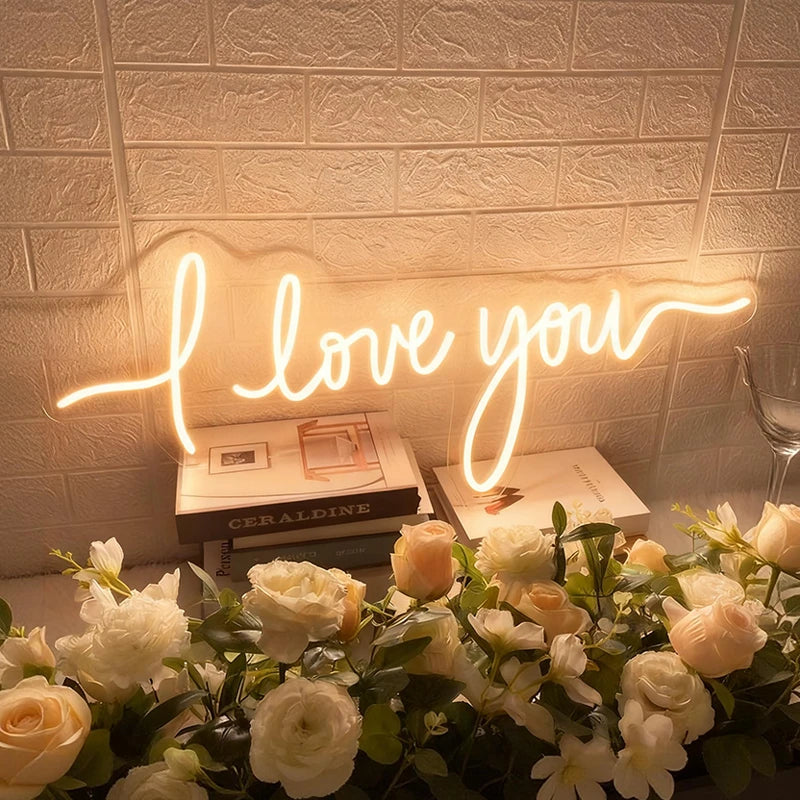 Neon sign saying 'I love you' with flowers and books in the background.