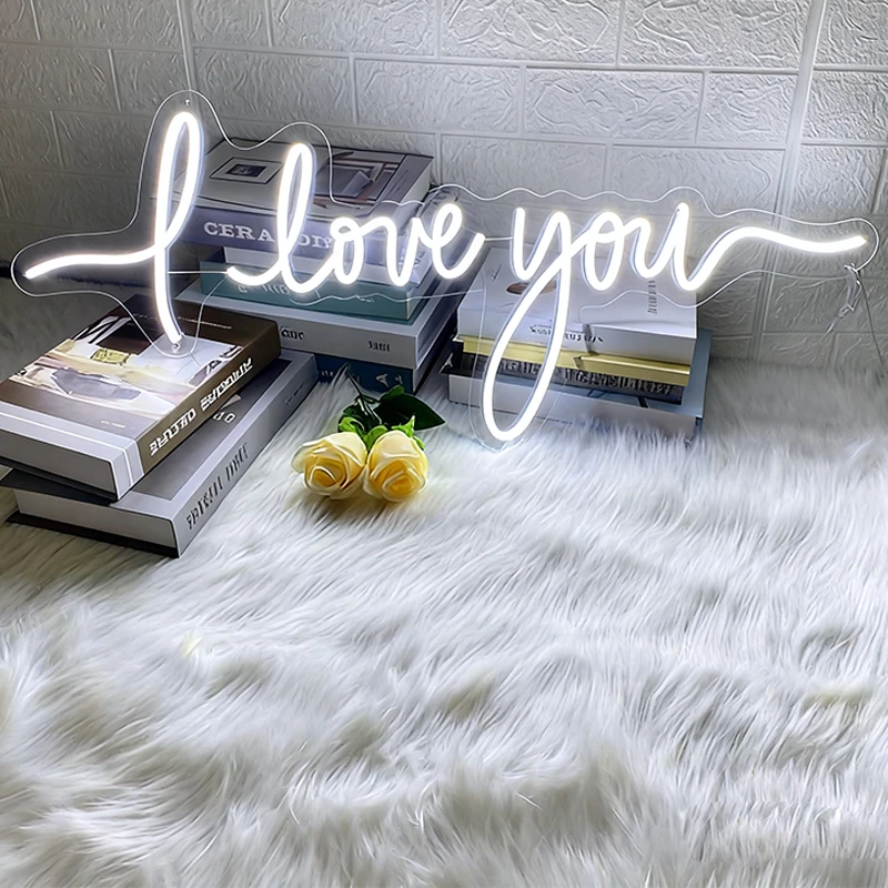 Neon sign saying 'love you' on a white fur surface with books and flowers.