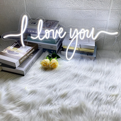 Neon sign saying 'love you' on a white fur surface with books and flowers.