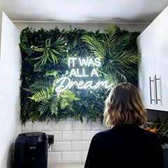 Neon sign with 'It was all a Dream' text surrounded by green foliage, person standing in front.