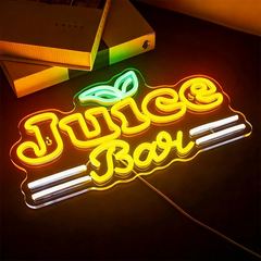 A high-angle, top-down view of a "Juice Bar" neon sign glowing brightly on a dark surface. The word "Juice" is in a bold lemon yellow font, topped with a green leaf icon, lemon yellow "Bar" is written in a cursive script between white horizontal accent lines. 