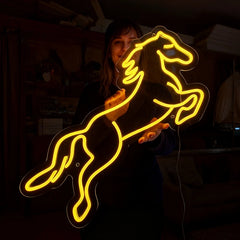 Person holding a neon horse sign with lemon yellow color in a dark setting