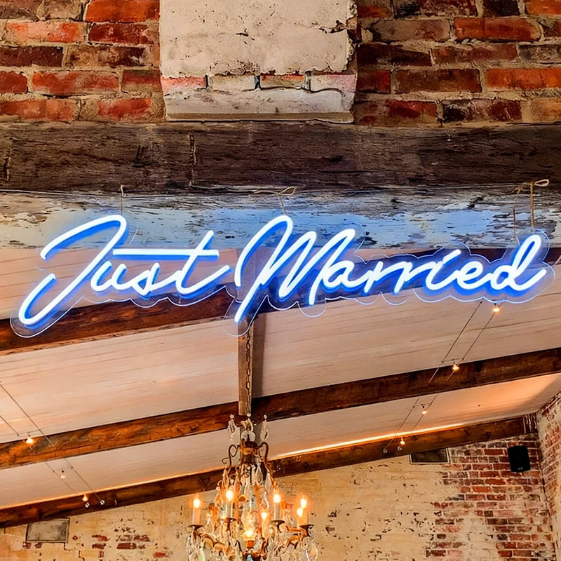 Neon sign reading 'Just Married' in a rustic setting with brick walls and a chandelier.