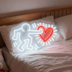 Neon sign of a person holding a heart on a pillow with bedding in the background