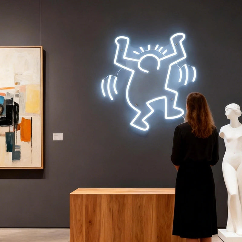 Woman looking at a neon artwork of a keith haring dancing man on a dark wall in an art gallery.