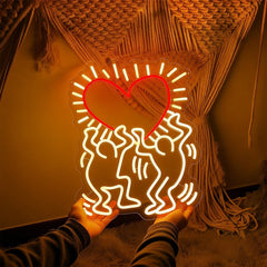 Neon light shaped like a heart with two people embracing, held against a textured wall.