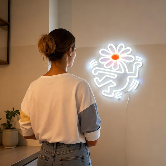 Person standing in front of a neon light shaped like a flower head with human body on a wall.