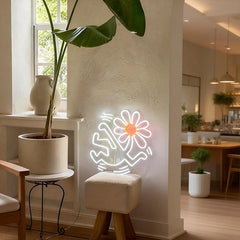 Neon flower head sign on a white wall in a home interior with plants and furniture.