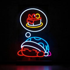 Neon sign of a kirby cartoon character with a cake in a thought bubble on a black background