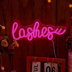 Neon sign with the word 'lashes' on a wooden background with flowers and a calendar.
