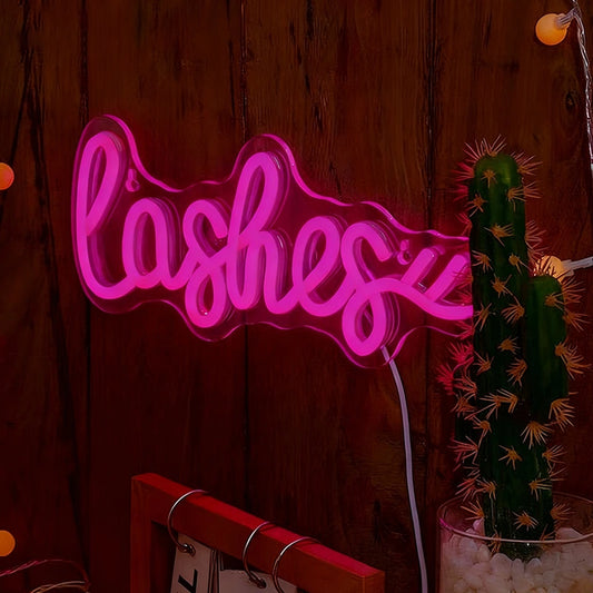 Neon sign with the word 'lashes' on a wooden wall with a cactus plant.