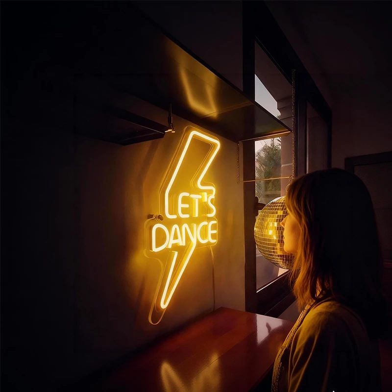 A person looking at a neon sign with 'Let's Dance' text.