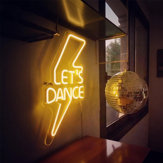 Neon sign with 'Let's Dance' text and disco ball in a dimly lit room