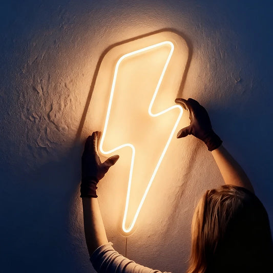 Warm white neon lightning bolt light fixture on a textured wall with hands reaching towards it.
