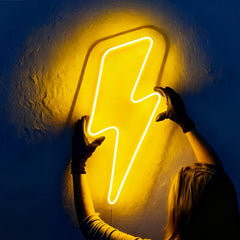 Lemon yellow neon lightning bolt sign being held by a person against a dark background