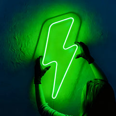 Person holding a green neon lightning bolt sign against a dark wall