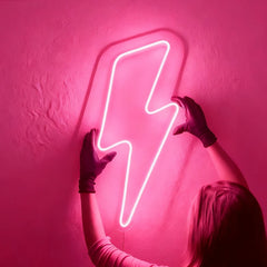 Person holding a hot pink neon lightning bolt sign against a pink wall