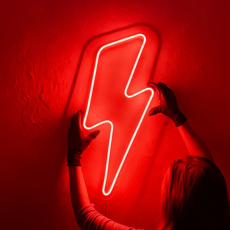 Person holding a red neon lightning bolt sign against a dark wall