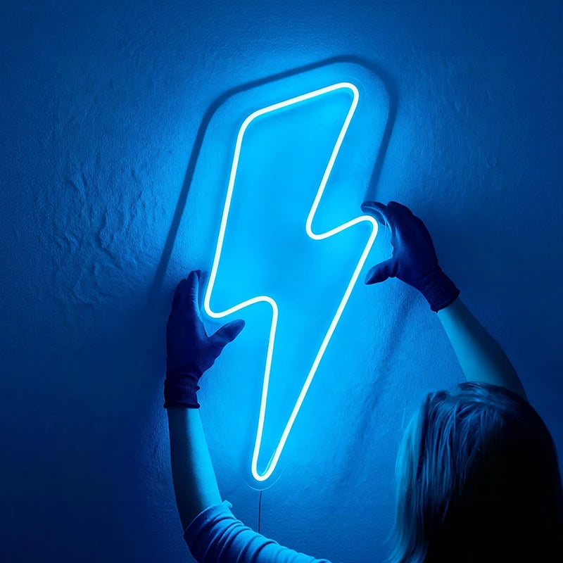Person holding a blue neon lightning bolt sign against a dark wall