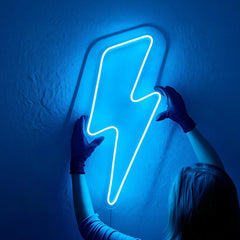 Person holding a blue neon lightning bolt sign against a dark wall