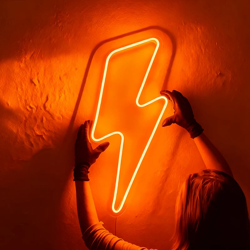 Person holding an orange neon lightning bolt sign against a dark wall