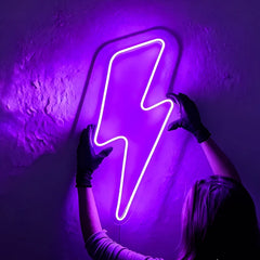 Person holding a purple neon lightning bolt sign against a dark wall