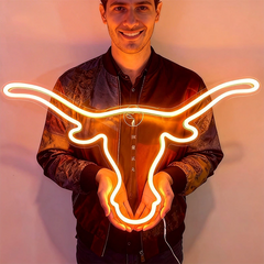 Man holding a neon sign of a bull's head against a plain background