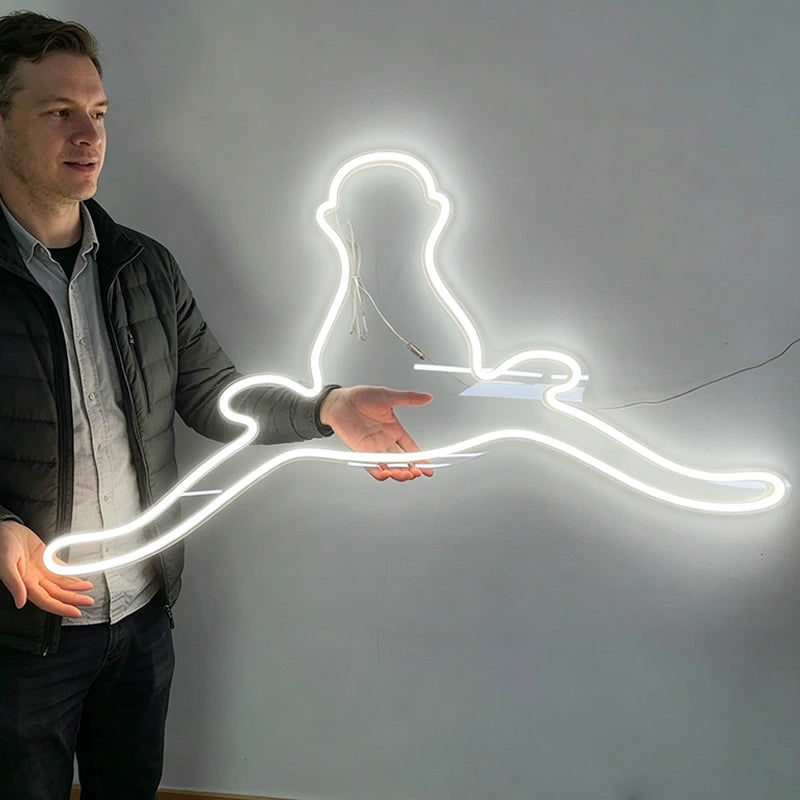 A man stands beside a glowing white neon-style light shaped like a longhorn bull, shown against a plain gray wall.