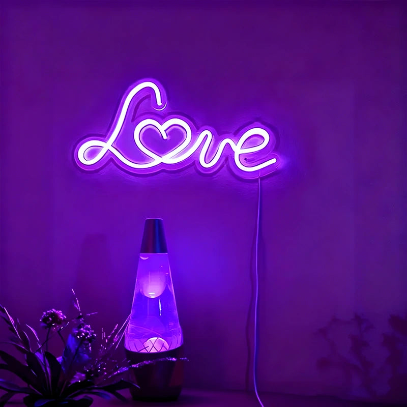 Neon sign with 'Love' on a purple wall with a lava lamp and plants below.